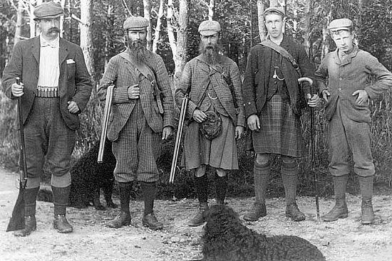 Black and white photo of bearded men with shotguns, some wearing kilts