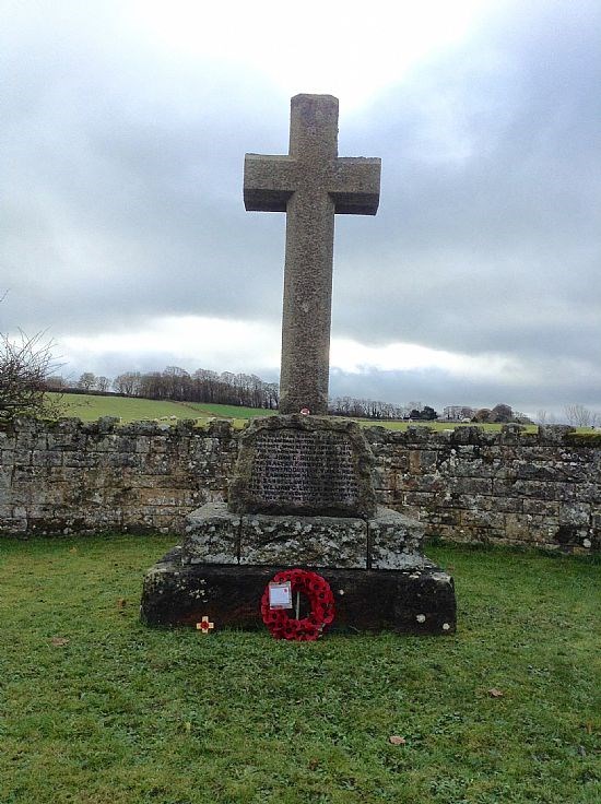 Stone cross with wreath of poppies in front of it.