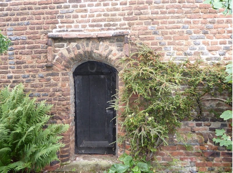 A doorway into a red brick building with initials F to the left and W to the right done in black brick