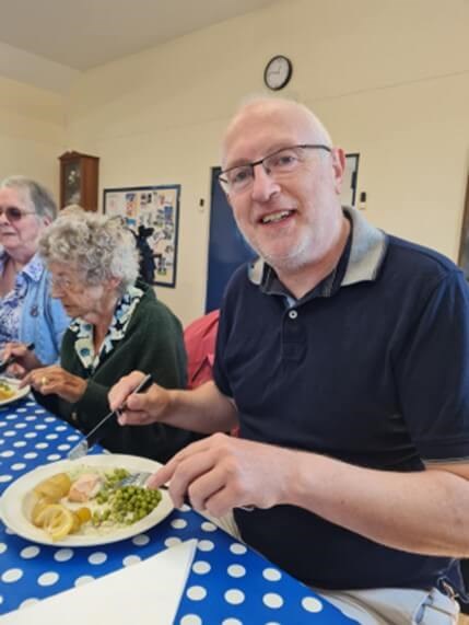 People sitting at a table and eating, one person is looking at the camera and smiling